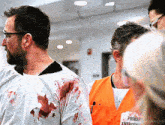 a man with blood on his shirt is wearing an orange vest with the word emergency on it