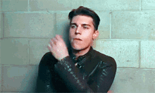a young man in a leather jacket is clapping his hands against a brick wall