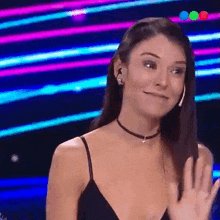 a woman wearing a choker and earrings is waving her hand in front of a colorful background .