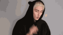 a man with blonde hair is wearing a black hoodie with ears on the hood .