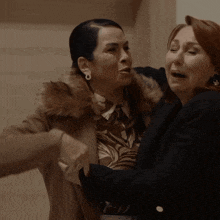 a woman in a fur coat is hugging another woman in a black coat