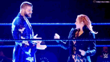 a man and a woman are standing in a wrestling ring shaking hands .
