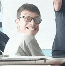 a young man wearing glasses is sitting at a desk and smiling