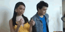 a man and a woman are standing next to each other holding hands . the woman is wearing a yellow top .