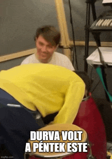 a man in a yellow sweater is kneeling down next to a drum .