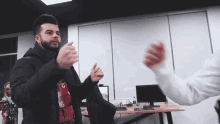 a man with a beard is giving a high five to another man while standing in front of a desk .