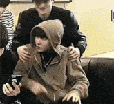 a man in a hoodie is sitting on a couch with a cell phone .