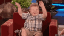 a young boy is sitting in a chair with his hands in the air .