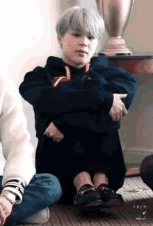 a person is sitting on the floor with their legs crossed and their arms around their chest
