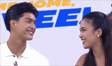 a man and a woman looking at each other in front of a sign that says " welcome "