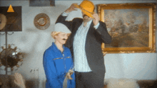 a man in a suit and a woman in a blue shirt are standing in front of a framed painting