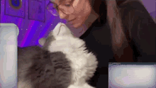 a woman wearing glasses is holding a cat in her arms .