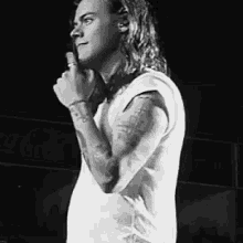 a black and white photo of a man with long hair holding a microphone in his hand .