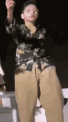 a young man in a camouflage shirt and khaki pants is dancing on a stage .