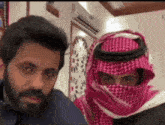 a man with a beard and a scarf on his head is standing next to another man .