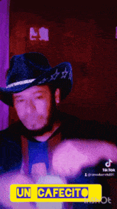 a man wearing a cowboy hat is holding a bottle with a yellow sign that says " un cafecito "