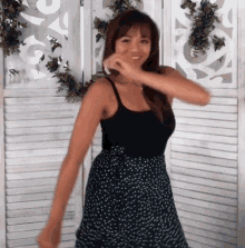 a woman in a black tank top and polka dot skirt is dancing in front of a screen