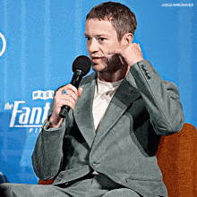 a man in a suit is holding a microphone in front of a blue background that says the fantastic