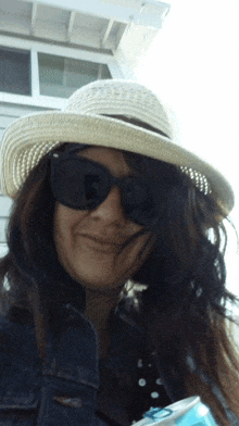 a woman wearing a hat and sunglasses is holding a can
