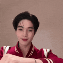 a young man in a red jacket is making a heart shape with his hands and smiling .
