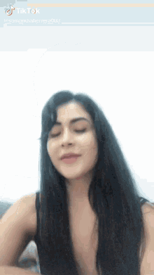 a woman with long black hair is making a funny face on a tiktok video .