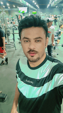 a man taking a selfie in a gym wearing a shirt that says muinow on it