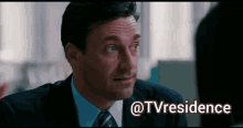 a man in a suit and tie is talking to another man with the words @tvresidence behind him