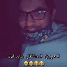 a man wearing glasses and a scarf has arabic writing on his shirt