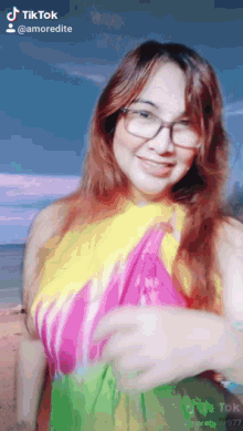 a woman wearing glasses and a tie dye top is smiling for a tik tok video