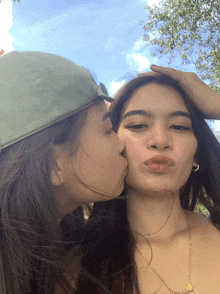 a woman kisses another woman on the cheek while wearing a green hat