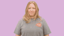 a woman with long blonde hair is wearing a grey shirt that says ' a ' on the back
