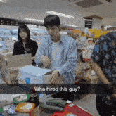 a man in a blue shirt is standing in front of a box that says who hired this guy on it