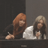 two women are sitting next to each other and one has a cell phone in her hand .