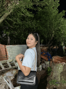 a woman standing in front of a fence with a black purse on her shoulder