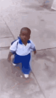 a little boy in a white shirt and blue pants is running down a sidewalk