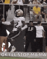 a football player with the number 12 on his jersey is jumping in the air while holding a football .