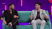 two men are sitting on a couch with a purple background and the word rtve in the corner