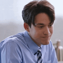 a man in a blue shirt and tie is smiling and looking at the camera .