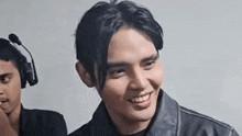 a man wearing headphones and a leather jacket is smiling and looking at the camera .