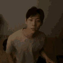 a man in a white t-shirt is scratching his head with his hand .