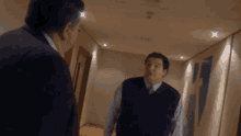 two men are standing in a hallway talking to each other