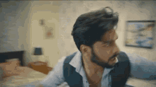 a man with a beard is sitting on a bed in a room .