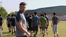 a man in a grey shirt is standing in front of a group of people walking in a field .