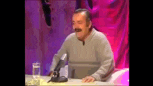 a man sitting at a table with a microphone and a glass of water .