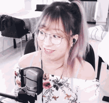 a woman wearing glasses and ear buds stands in front of a microphone