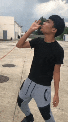 a young man in a black shirt and grey sweatpants is drinking water from a bottle