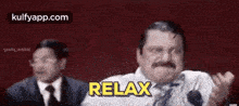 a man with a mustache is sitting in front of two other men and says relax