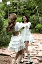 two women in white dresses are hugging each other on a rocky path .