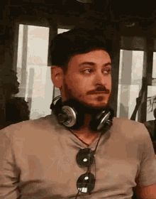 a man with a beard wearing headphones and sunglasses is sitting in front of a window .