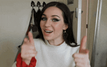 a woman in a white sweater giving a thumbs up sign